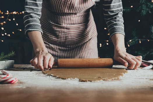 Merry Christmas, Happy New Year. Gingerbread cooking, cake or strudel baking. A young woman or mother rolls out the dough with a rocking chair for extruding and cutting out cookies. High quality photo