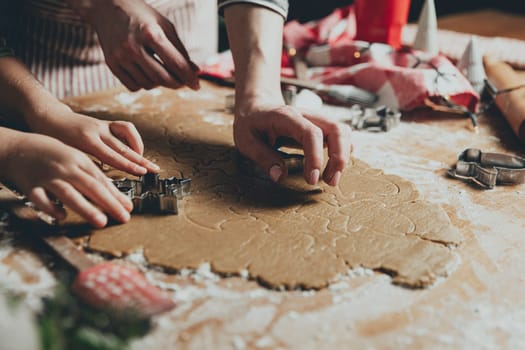 Merry Christmas, Happy New Year. Gingerbread cooking, baking. Mom and daughter make cookies, cut out different shapes of cookies using cutting metal mold on wooden table at kitchen. High quality photo