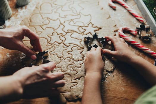 Merry Christmas, Happy New Year. Gingerbread cooking, baking. Mom and daughter make cookies, cut out different shapes of cookies using cutting metal mold on wooden table at kitchen. High quality photo