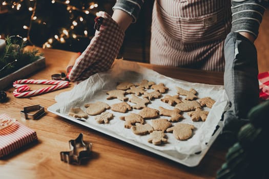 Merry Christmas, Happy New Year. Gingerbread cooking, cake or strudel baking. A young woman or mother holds deco, holding sheet with ready-made baked cookies in her gloves hands. High quality photo