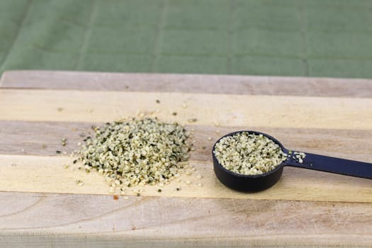 One pile and one tablespoon of organic shelled hemp seeds on a wood cutting board close-up. One pile and one tablespoon of shell-less organic hemp seeds, or hemp hearts on a wooden cutting board.