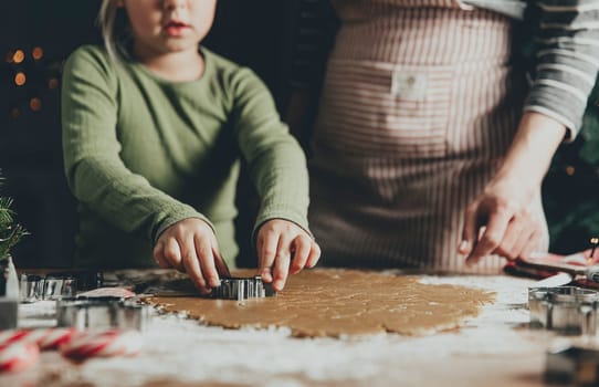 Merry Christmas, Happy New Year. Gingerbread cooking, baking. Mom and daughter make cookies, cut out different shapes of cookies using cutting metal mold on wooden table at kitchen. High quality photo