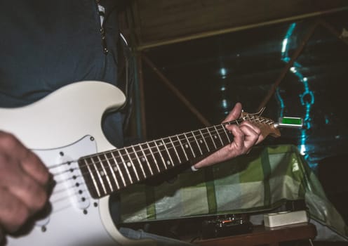 A man plays a white electric guitar