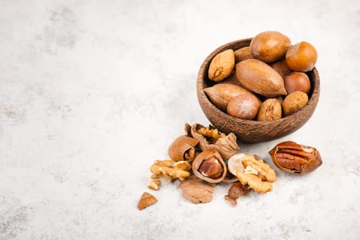 Mix of nuts, like hazelnuts, walnuts in a wooden bowl on a textured background, empty copy space for text