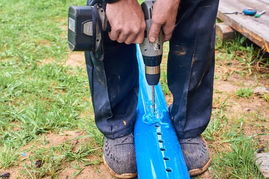drill holes in the plastic blue pipe with a screwdriver outdoors. High quality photo