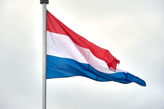 The flag of the Netherlands hangs on a metal flagpole. High quality photo