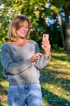 A woman in a park in the summer speaks during a video call on the phone. High quality photo