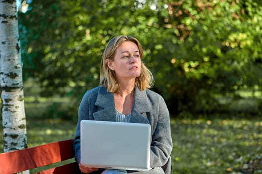 A woman with a laptop is sitting on a park bench on a sunny summer day. High quality photo
