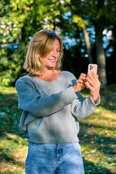 A woman in a park in the summer speaks during a video call on the phone. High quality photo