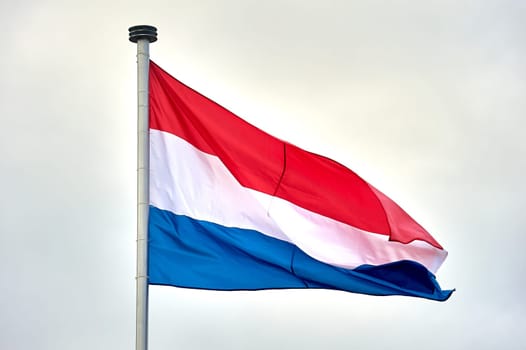 The flag of the Netherlands hangs on a metal flagpole. High quality photo