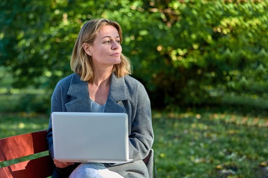 A woman with a laptop is sitting on a park bench on a sunny summer day. High quality photo