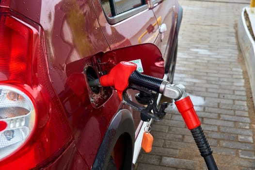 the red pistol is inserted into the gas tank of a red passenger car for refueling with gasoline. High quality photo
