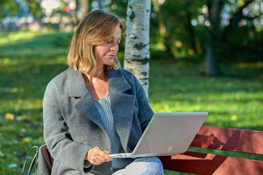A woman with a laptop is sitting on a park bench on a sunny summer day. High quality photo
