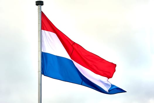 The flag of the Netherlands hangs on a metal flagpole. High quality photo