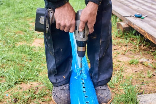 drill holes in the plastic blue pipe with a screwdriver outdoors. High quality photo