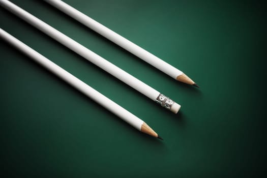 Three blank white pencils on green background.
