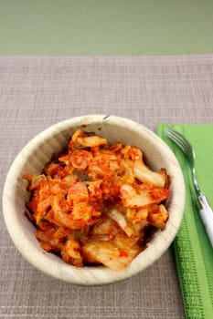In a wooden bowl ready to eat with a fork is fermented kimchi made with napa cabbage and radish. Flavorful fermented napa cabbage with radish and aromatic seasonings kimchi recipe in a wooden bowl.