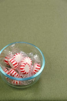 Individually wrapped with clear plastic white and red peppermint hard candy discs in a glass bowl on a green tablecloth. White and red peppermint hard candy in a clear bowl on a green tablecloth.