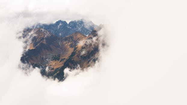 Mysterious mountains covered by a thick fog in nature. A see through window to a slopes and valleys of High Tatras national park, Slovakia. Horizontal landscape with rocky hills behind a mist.