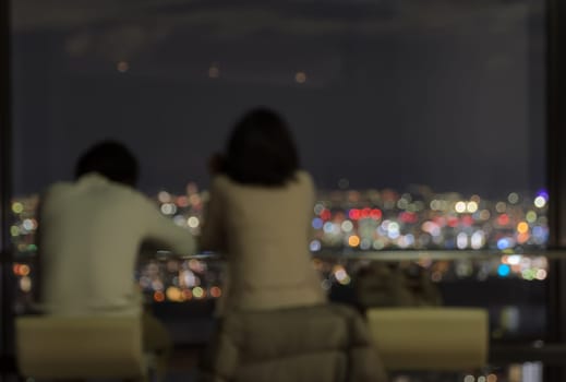 Blur couple sitting on skyscraper observatory overlooking the city aerial view at night
