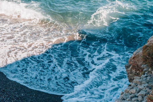 Waves, rock and black sand on Kamari Beach, Santorini, Greece.