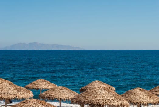 Straw beach umbrellas against the blue sea and sky.