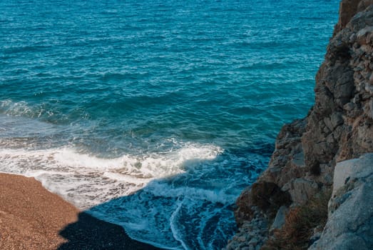 Top view of the black sand, sea, waves and rock at Kamari Beach, Santorini.