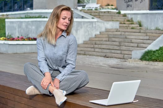 A woman with a laptop sits on a wooden platform, works online. High quality photo