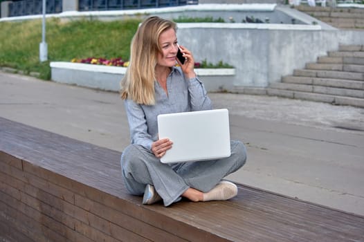 A woman with a laptop sits on a wooden platform, works online. High quality photo