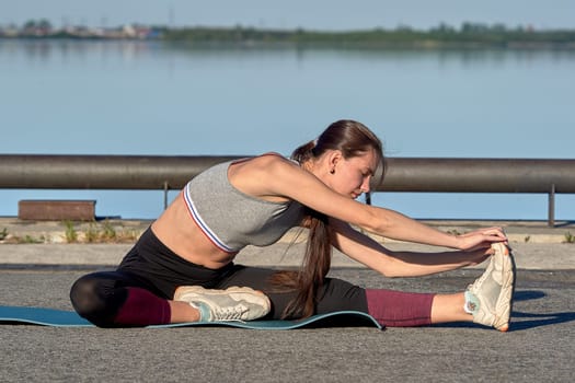 A young woman does a warm-up on the pier in the early morning, against the background of the river. High quality photo