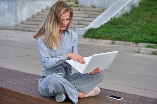 A woman with a laptop sits on a wooden platform, works online. High quality photo