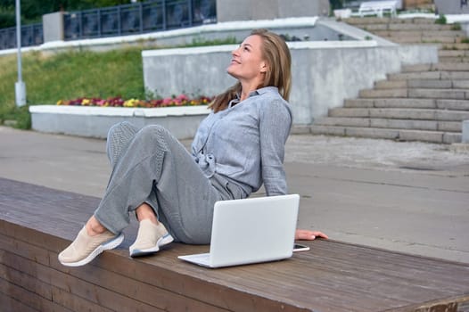 A woman with a laptop sits on a wooden platform, works online. High quality photo