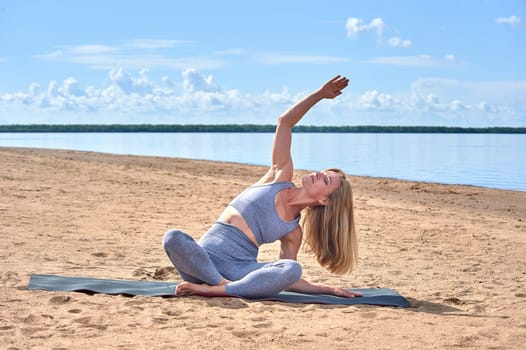 A woman does yoga on a sandy beach against the background of a river. High quality photo