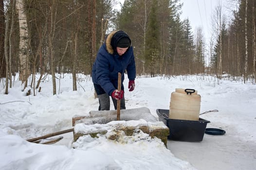 A man draws water from a spring in a plastic barrel in winter. High quality photo