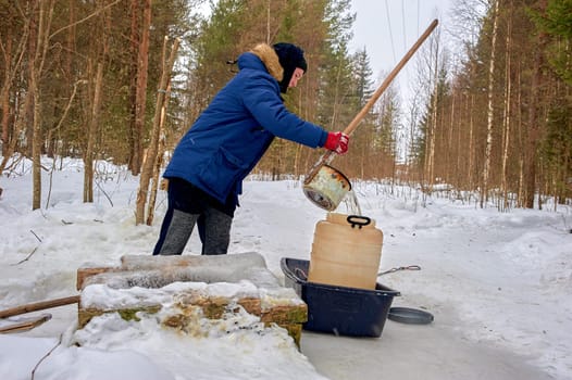 A man draws water from a spring in a plastic barrel in winter. High quality photo