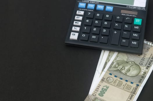 Indian Rupee placed under a calculator on table. Isolated on black background.