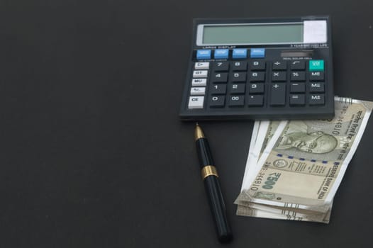 Indian Rupee placed near calculator and a pen on table. Isolated on black background.