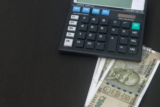Indian Rupee placed under a calculator on table. Isolated on black background.