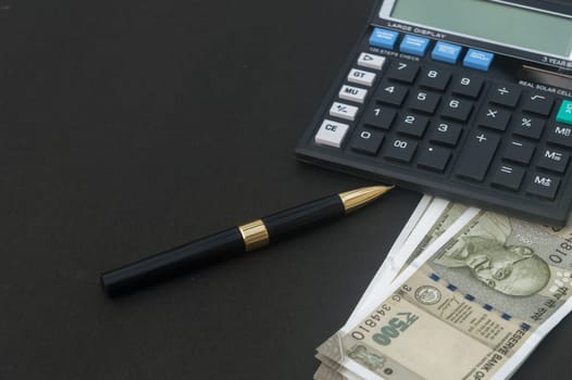 Indian Rupee placed near calculator and a pen on table. Isolated on black background.