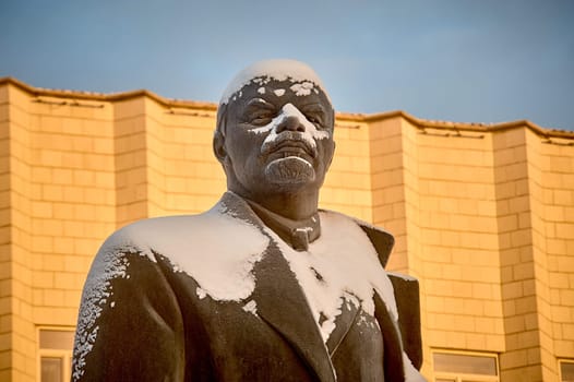 bust of Vladimir Lenin on the background of a white building dusted with snow