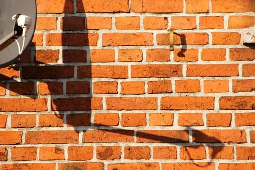 A satellite dish on a brick building casts a shadow.