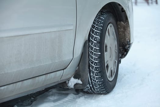 winter snowy road, car wheel with winter studded tires low angle view