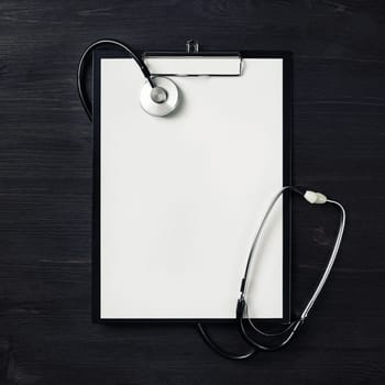 Blank clipboard with stethoscope on wood table background. Top view. Flat lay.