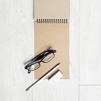 Photo of blank kraft notepad, pencil, eraser and glasses on light wooden background. Responsive design mockup.