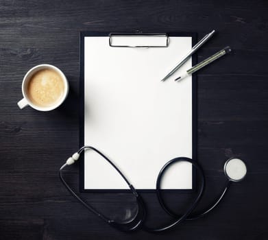 Doctor's medical supplies. Blank clipboard, stethoscope, badge, thermometer, pen and coffee cup on wood table background. Top view. Flat lay.