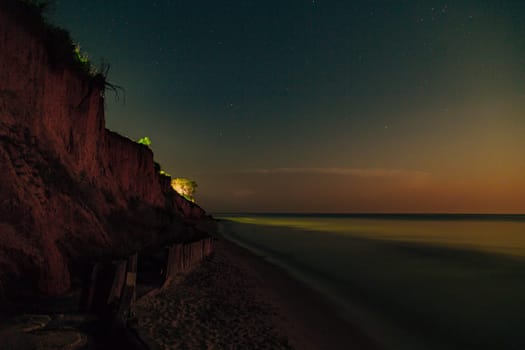 Golden sunset on the shores of the calm sea. Starry dark blue sky with stars.