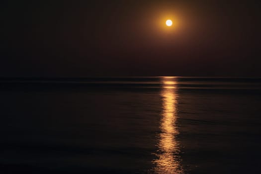 The Full Red Moon Shines Brightly in the Sky on a Dark Night Over the Calm Sea. Beautiful Moon Path on the Water.