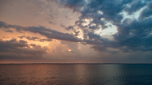 Beautiful Landscape of the Sunset on the Beach. Calm Weather with Dark Clouds in the Golden Sky Reflected in the Water.