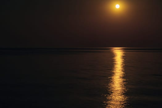 The Full Red Moon Shines Brightly in the Sky on a Dark Night Over the Calm Sea. Beautiful Moon Path on the Water.
