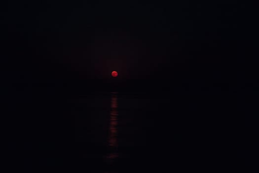 Full Red Moon Glows Brightly in the Sky on a Dark Night Over the Calm Sea with Copy Space.